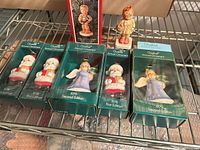 Overview of five boxed Goebel Annual Angel ornaments and one loose angel figurine on metal shelf
