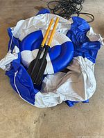 Deflated blue and white circular float with removable center and two yellow-shaft black-blade paddles
