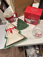 All items arranged: red mug, boxed serving bowl, stemless wine glass, two nested white tree platters, green tree plate