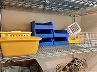Shelf with large yellow bin, four blue stackable bins, white wire basket, white grid crate