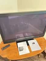 Front view of Panasonic plasma TV on stand with remote and manuals visible