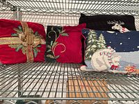 Four holiday pillows on wire shelf: red velvet ribbon bow, red velvet vine embroidery, partial black moose pillow, blue polar bear needlepoint
