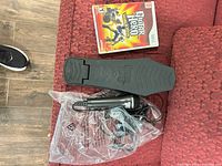 Foot pedal, microphone, Wii Guitar Hero game case and cords on red sofa