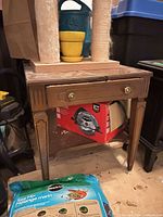 Full view of brown veneer end table showing drawer, hardware, legs, and lower shelf