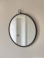 Front view of round mirror showing black frame, reflective surface, and gold/brass loop