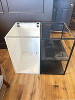 White cabinet carcass beside black metal frame shelf unit, showing overall structure and condition