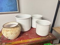 Three white stoneware crocks and one ivory planter with gold rim on red table