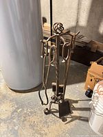 Full view of wrought iron fireplace tool set showing stand with poker, shovel and tongs