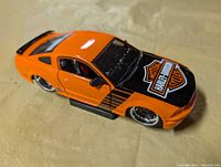 Passenger front angle of orange Ford Mustang diecast with Harley-Davidson hood graphic