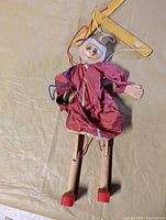 Full view of marionette showing wooden limbs, pink outfit and control bar