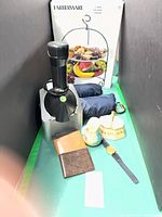 Group shot of entire lot including Yonanas appliance, Farberware server box, rolled jackets, wallets, watch, pitcher, basket