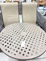 Round beige lattice-top patio table with two matching beige sling armchairs