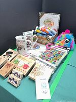 Overview of lot showing paint tubes in box, rubber stamps, sticker sheets, two ceramic mugs, plush pouch