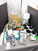 Group shot of entire lot showing coffee maker, mugs, garden shear box, power strips, hardware jars, adapters