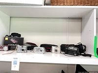 Shelf view showing five compact digital cameras, cases and one box