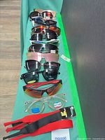 Row of eight eyewear pieces and two straps displayed on green cloth