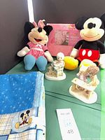 Group shot of both Disney plushes, both Precious Moments figurines, Mickey blanket and packaging