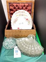 All items grouped: stack of floral china dinner plates inside lined wicker basket, pressed glass serving bowl and candy dish in front