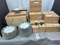 Stacked salad plates, soup bowls, salt & pepper shakers, covered jar and multiple sealed cardboard boxes with same pattern dinnerware