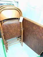 Stacked copper finish folding chairs and square folding table leaning against wall