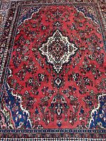 Full view of red Persian rug with blue borders and floral medallion