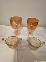 Front view of two amber goblets, creamer, sugar bowl on white cloth
