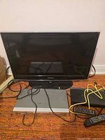 Front view showing Samsung 32-inch TV, DVD player, Blu-ray player, remote and cabling