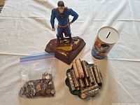 Overall lot: Superman plastic bank, Superman tin bank, bag of loose coins, platter of coin rolls