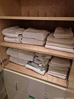 Two cabinet shelves loaded with folded white towels of different sizes