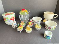 Group shot of all items: ceramic strawberry jar, glass jam jar with spoon, cream mug, three floral ramekins, five cheese/mouse toppers