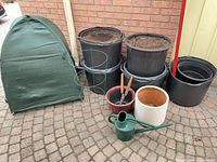 Lot overview showing green pop-up cover, tomato cage, black planters, shears and watering can