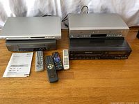 All three players, five remotes and manual on wooden surface