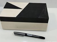 Closed box with marker for scale showing black and cream geometric lid
