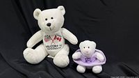 Large and small white plush teddy bears displayed on black backdrop