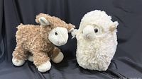 Brown and white plush sheep toys side by side on black backdrop
