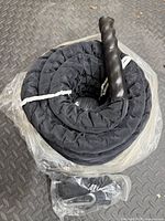 Coiled black battle rope in plastic with handle visible on floor mat
