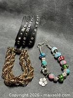 overview of three bracelets: black wrap, gold chain, charm with beads