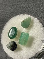 All four loose green emerald stones on white pad
