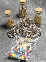 Overview of three corked glass bottles of gold-tone findings, silver-tone chain, bag of beads and charms