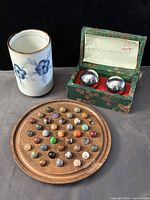Group shot of porcelain cup, solitaire board with marbles, Baoding balls in box