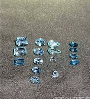 All 16 blue topaz gemstones arranged by cut and hue on dark background