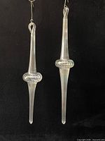 Full view of both iridescent glass icicle ornaments against black background