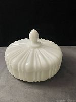 Covered milk glass candy dish, lid on, showing ribbed sides and finial