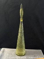 Full view of tall olive green glass decanter with stopper against black backdrop