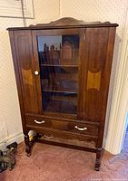 Front view of walnut china cabinet showing glass door, drawer, stretcher base