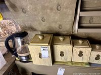 four wooden pineapple canisters with glass kettle on shelf