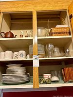 overall view of cupboard contents showing dishes, glasses, teapot, basket