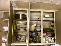 Open cupboard showing stock pot, roasting pan, plates, bowls, glass bottles, utensils
