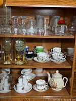 Cabinet shelves showing clock, glasses, cups, teapot, condiment set