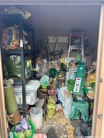 Overall view of packed shed showing tools, ladder, hose, shelves, bins, planters